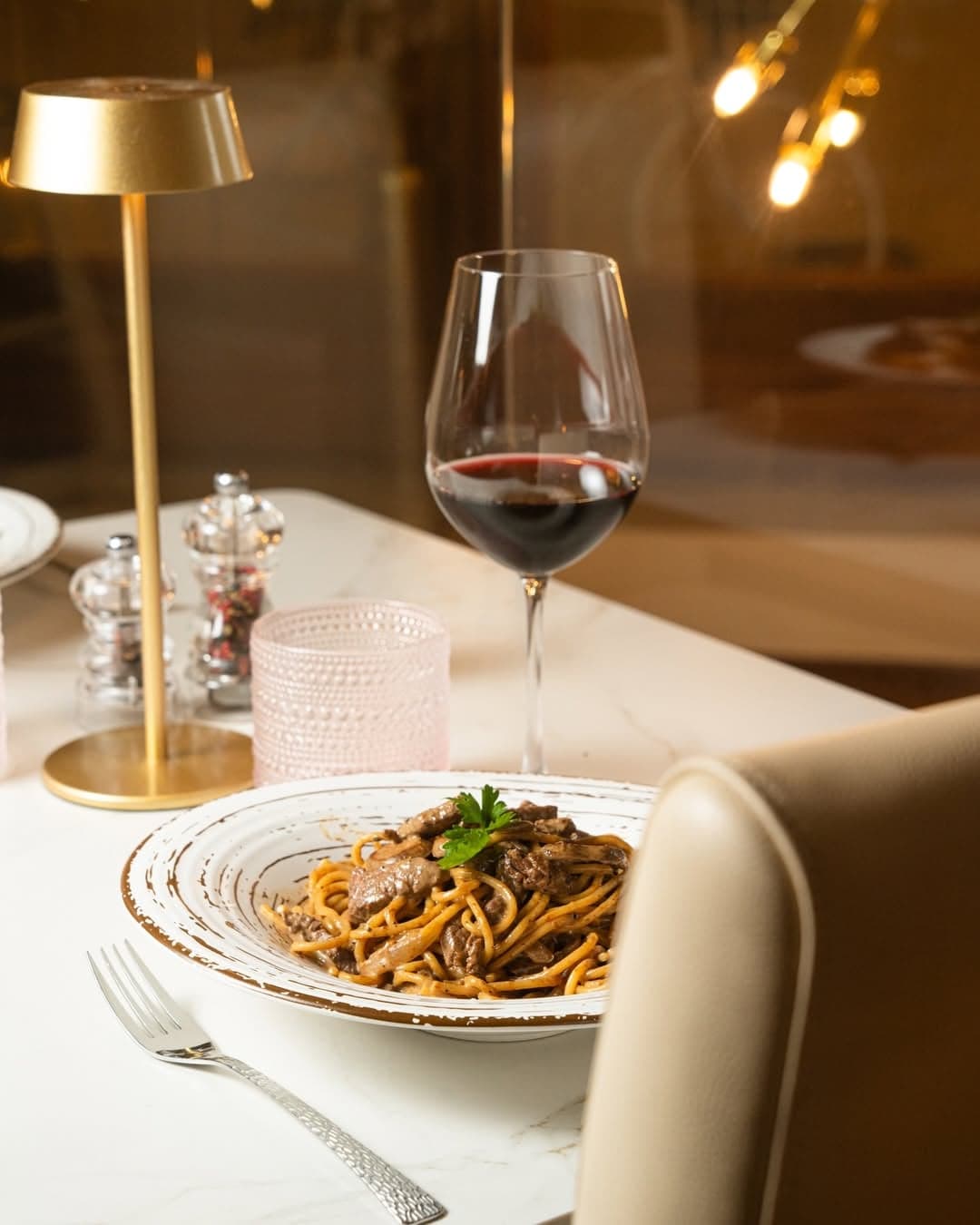 Pasta al ragú en mesa con lámpara dorada y vino