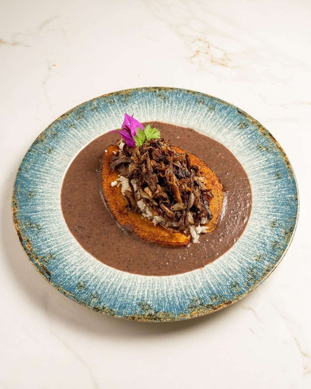 Tostón con ropa vieja sobre crema de frijoles negros